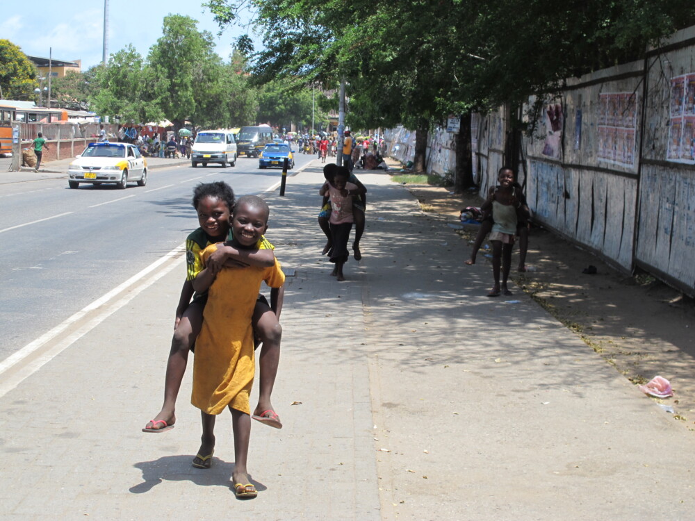 Six children playing piggyback with each other, walking down a street in Accra