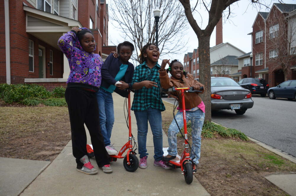Four girls with two scooters playing on a sidewalk