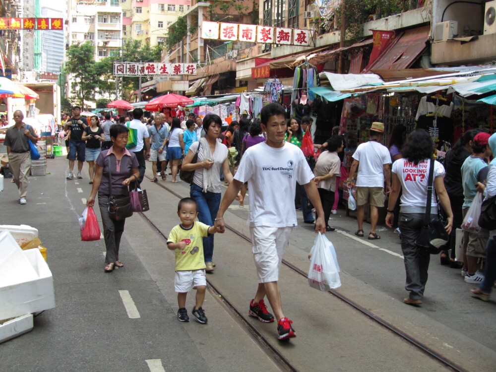 A man walking down a busy Hog Kong street holding the hand of a young child